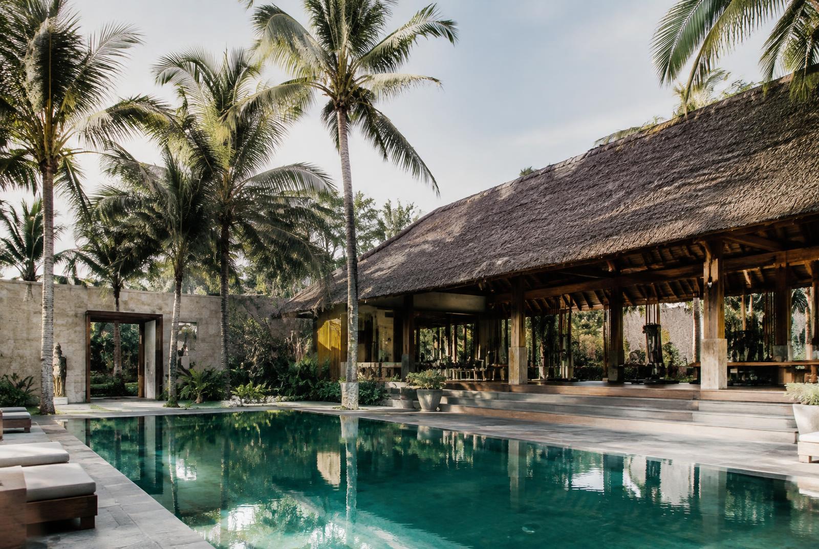 Tropical wellness pavilion with thatched roof beside a landscaped pool framed by palm trees